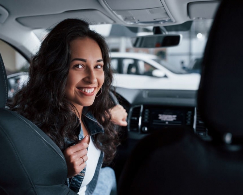 Positive emotions. Cute girl with black hair trying her brand new expensive car in the automobile salon.
